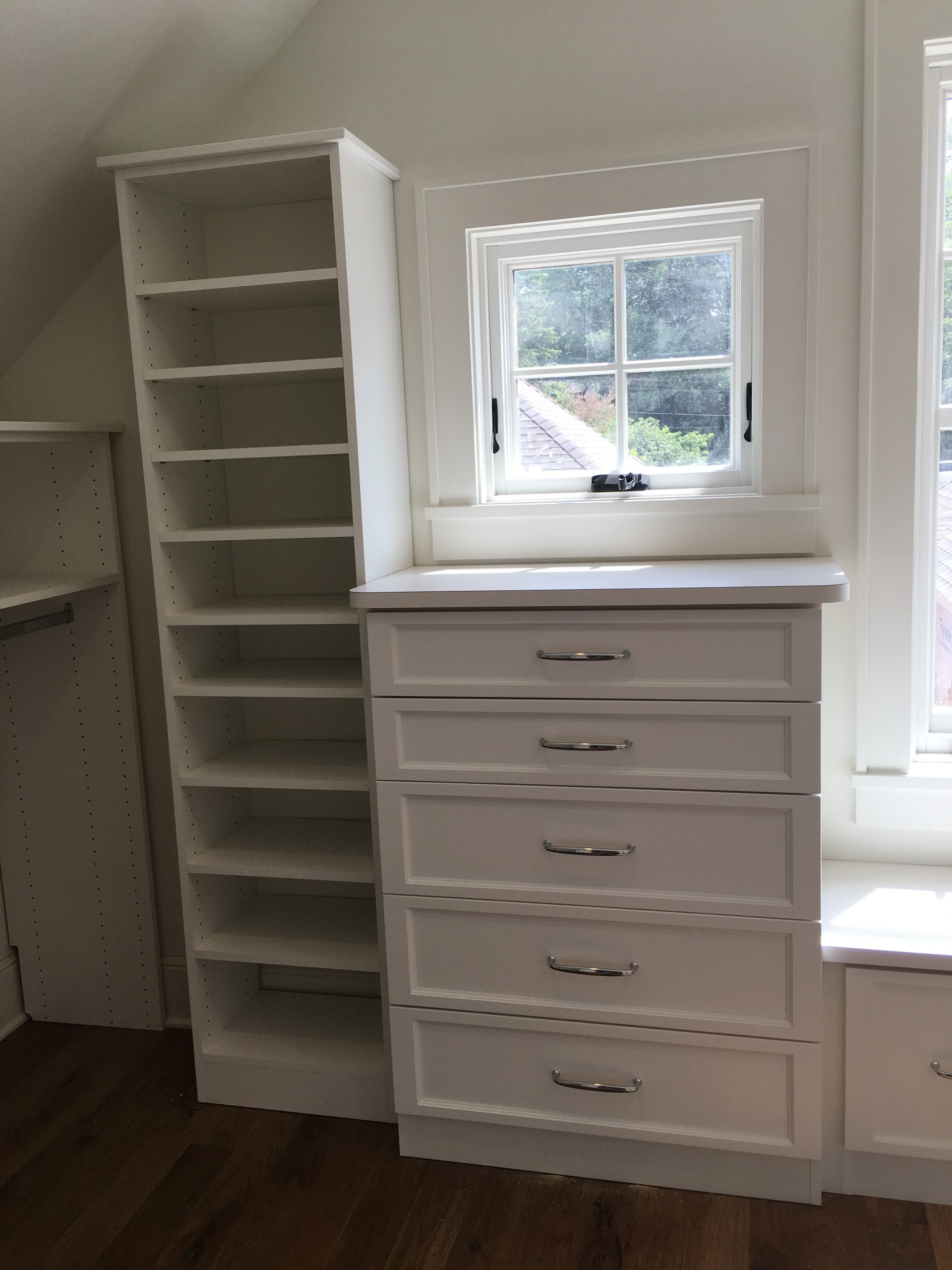 Closet built under a sloped ceiling with a built-in drawer bank and tall shoe shelving